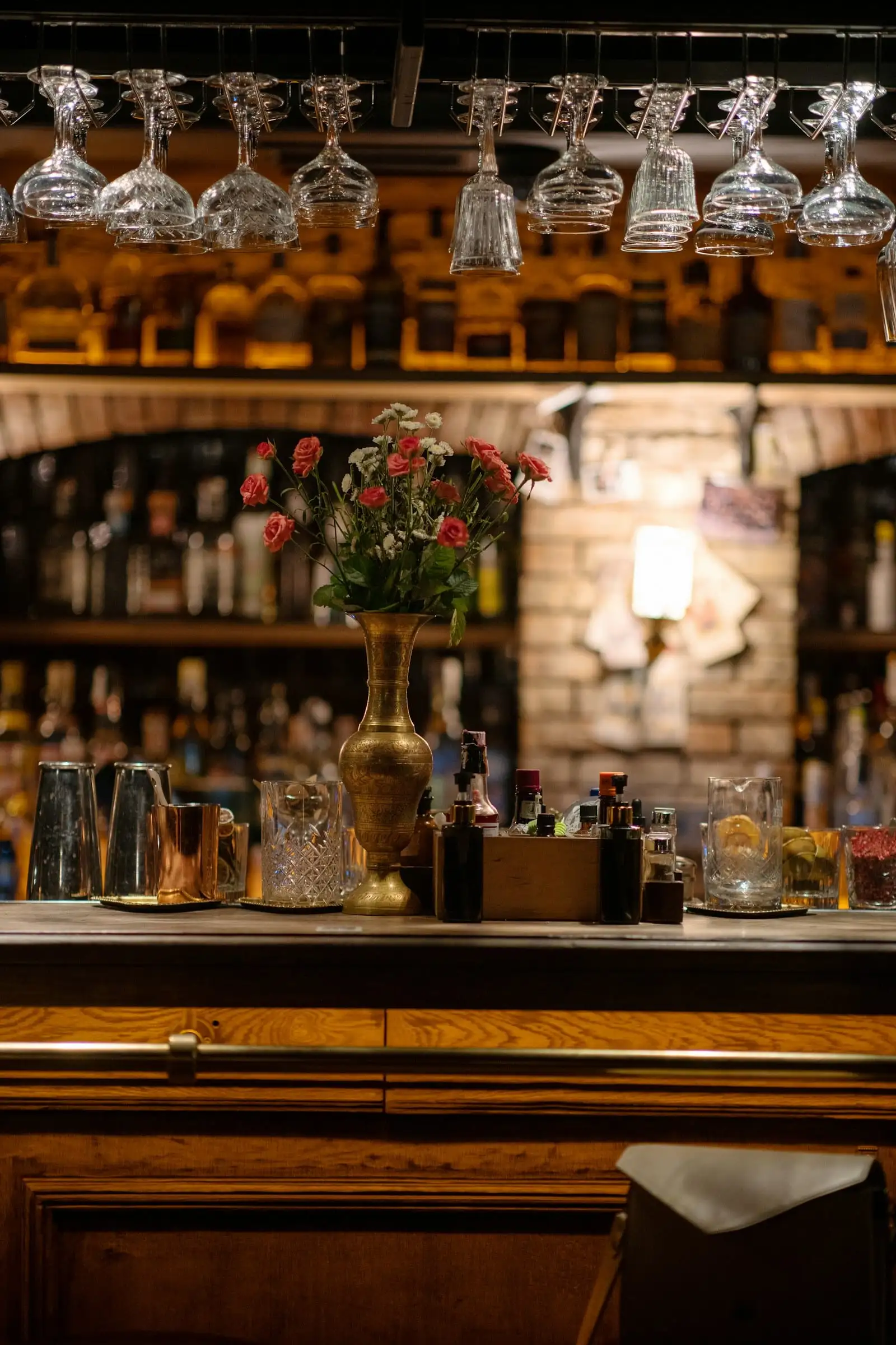 Barra de madera con botellas, copas colgadas y un jarrón con flores