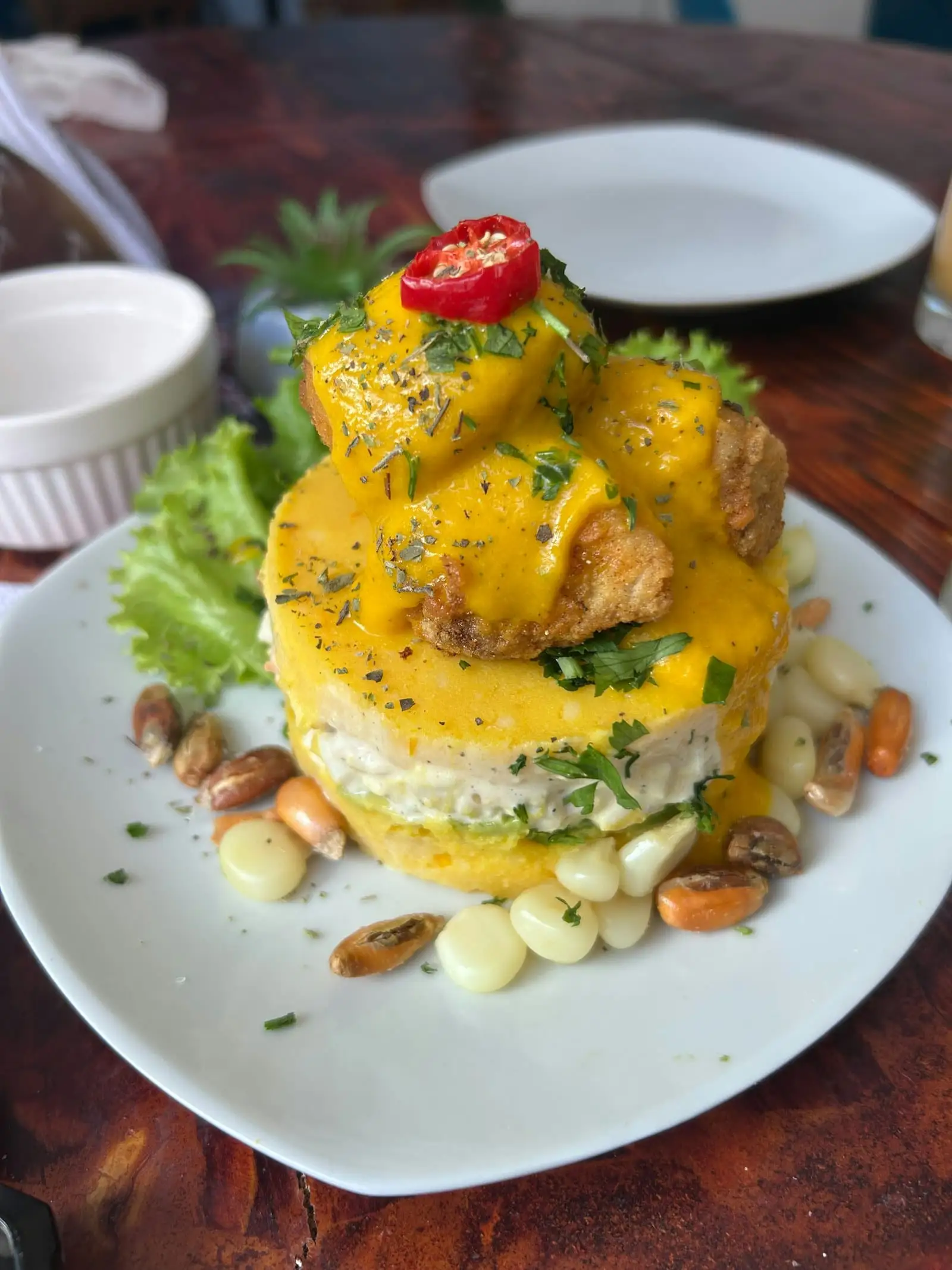 Causa en capas con pescado frito, crema amarilla y choclo