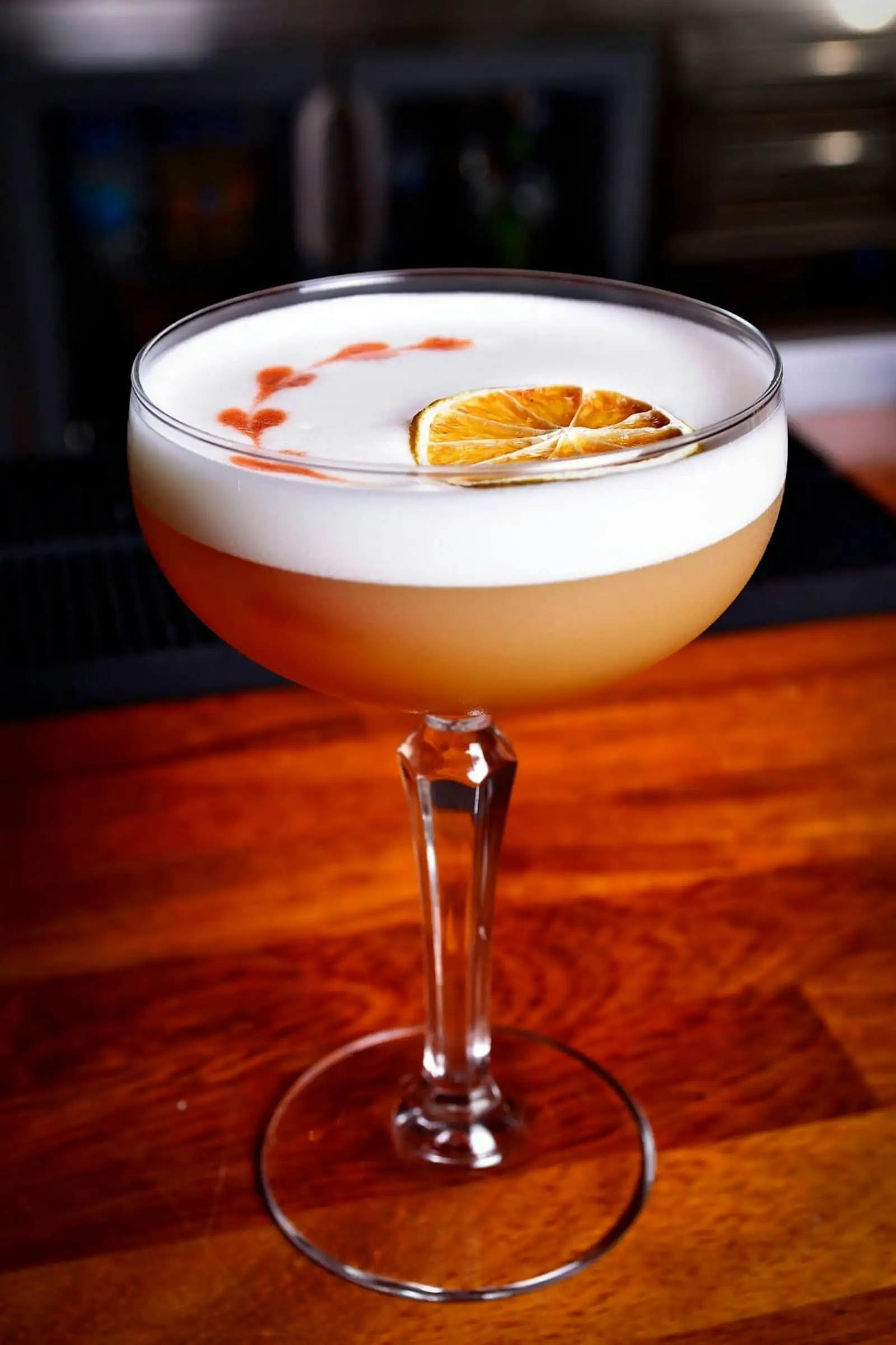 Pisco sour con espuma y una rodaja de naranja seca sobre la barra